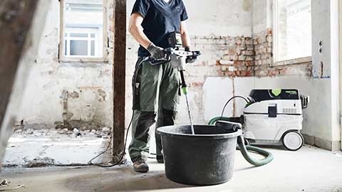 O meșteșugară se află pe un șantier și folosește un mixer Festool în combinație cu un aspirator.